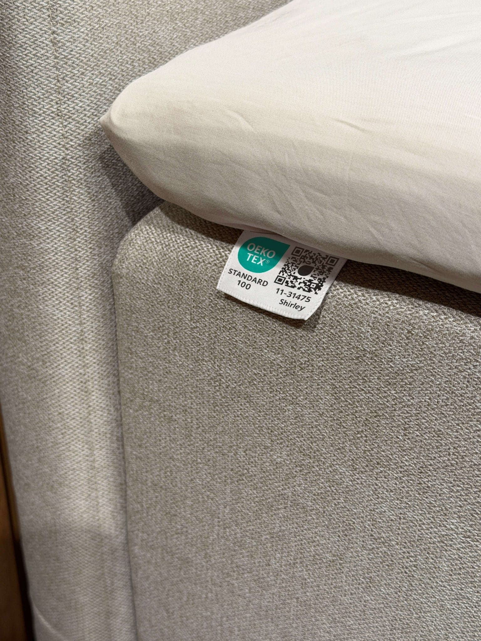 OEKO-TEX® STANDARD 100 etiketė, prisiūta prie smėlio spalvos lovos audinio po paklode